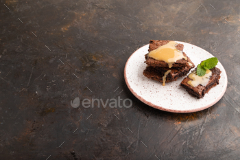 Chocolate brownie with caramel sauce with a cup of coffee on black concrete, side view, copy space.