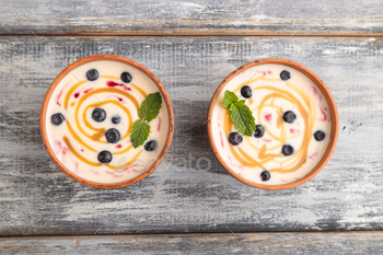 Yoghurt with bilberry and caramel in clay bowl on gray wooden, top view