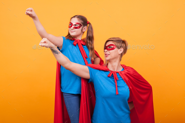 Mother and daughter dressed like heroins holding their fist in the air and looking away over yellow