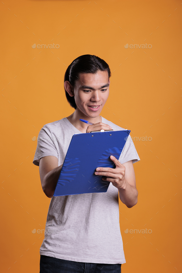 Smiling asian man taking notes in blue clipboard