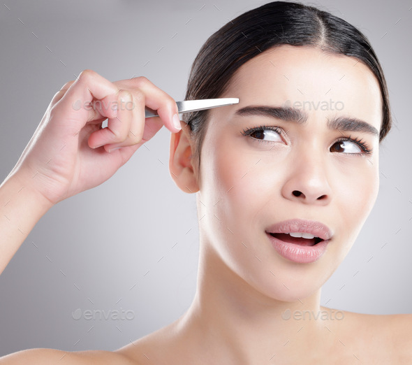 Studio shot of an attractive young woman plucking her eyebrows against