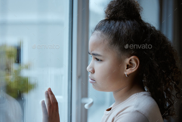 Shot of a little girl starting out of the window looking sad at home