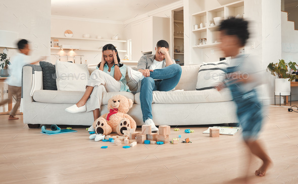 Shot of a young couple looking stressed at home while their kids play around them