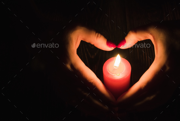 Female hands folded in the shape of a heart and a candle flame in the dark - Stock Photo - Images