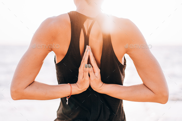 Young yogi woman practicing yoga, standing in sea with Namaste behind the back, working out wearing