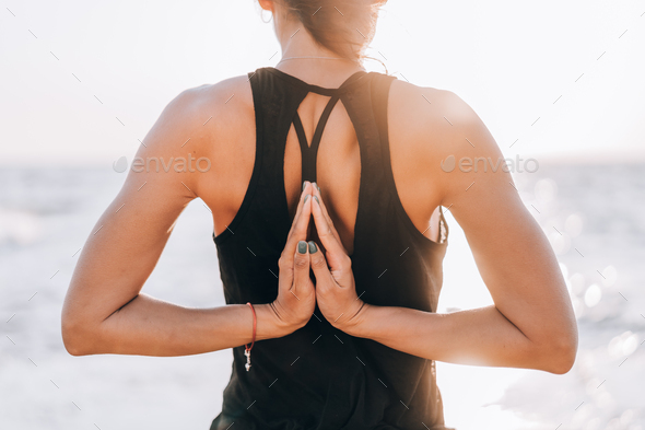 Young yogi woman practicing yoga, standing in sea with Namaste behind the back, working out wearing