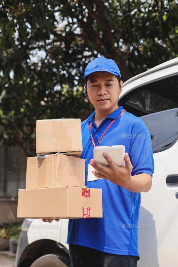 Courier checking smartphone while bring pile of cardboards