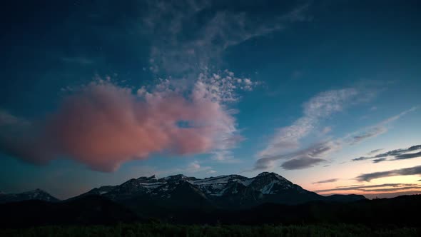 Time lapse of clouds lighting up at sunset over snow capped mountain alt