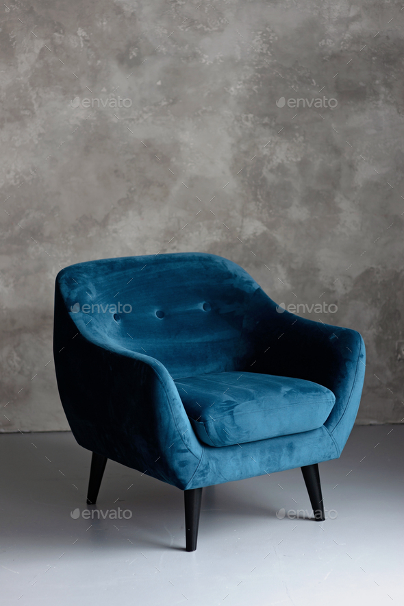 Classic blue velvet art deco armchair with wooden legs against a gray wall. Front view.