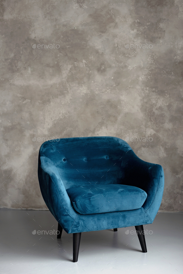 Classic blue velvet art deco armchair with wooden legs against a gray wall. Front view