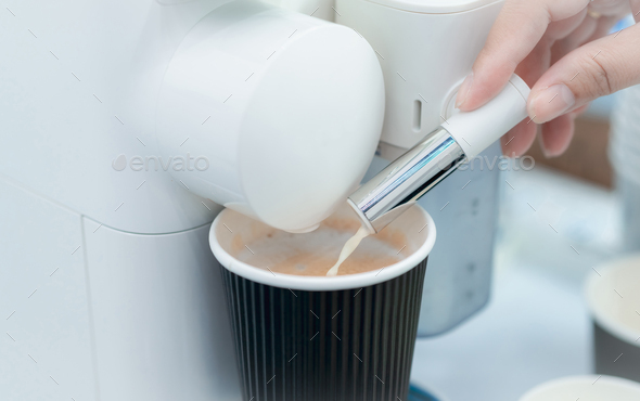 Woman making a cup of hot coffee with capsule coffee machine. Woman hand holding frothed milk