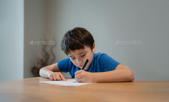 Kid doing homework,Child boy holding black pen writing on white paper
