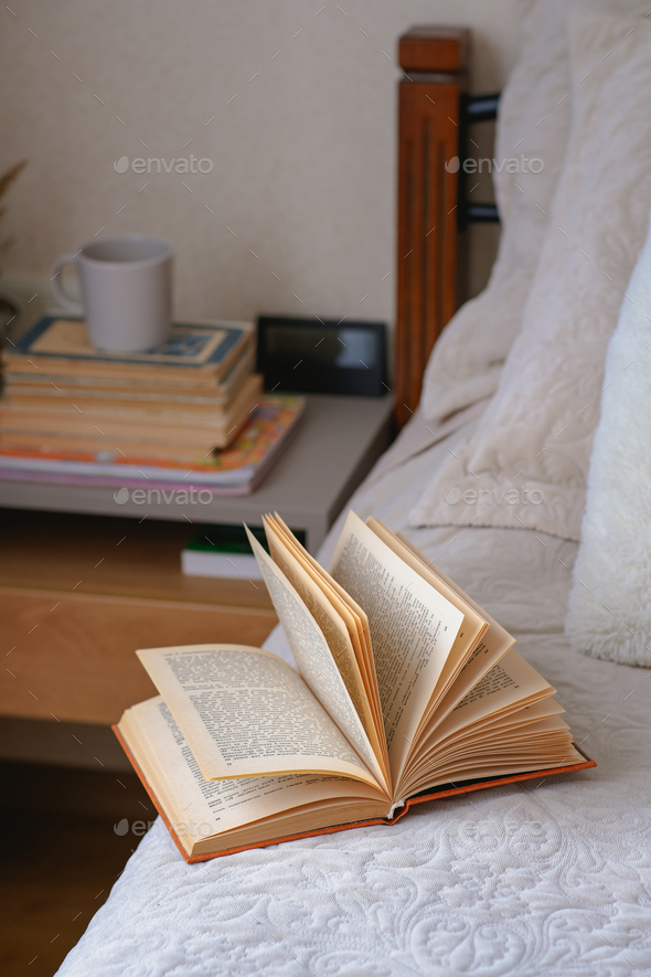 Old open book with yellow pages lies on a beige bed with pillows.  - Stock Photo - Images