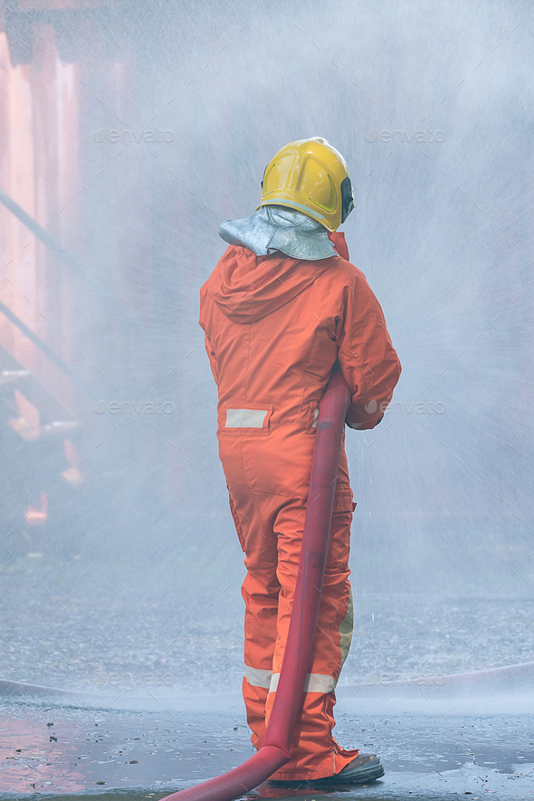 Fire man spray water from hose for fire fighting. Firefighter spraying