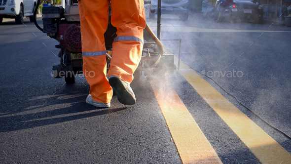 Road worker using thermoplastic marking machine to painting yellow lines on asphalt road