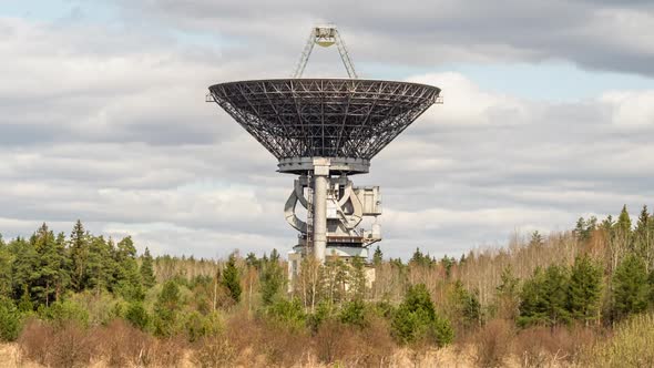A radio telescope above forest in front of coudy sky