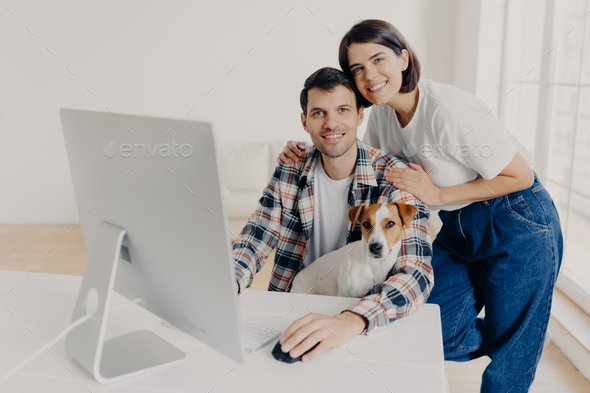 male freelancer works remotely at computer with dog, his affectionate wife embraces - Stock Photo - Images