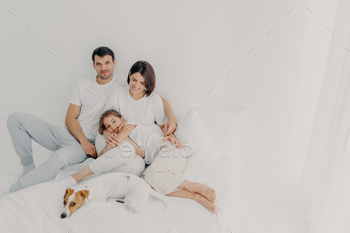 Happy family pose on white bed during weekend. Father, mother