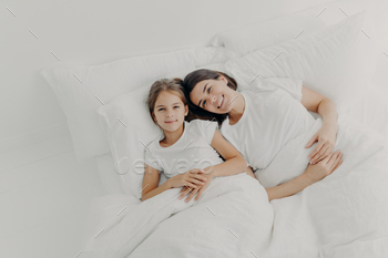 Top view of happy mother and daughter awake in good mood, feel relaxed