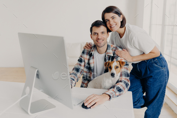 male freelancer works remotely at computer with dog, his affectionate wife embraces