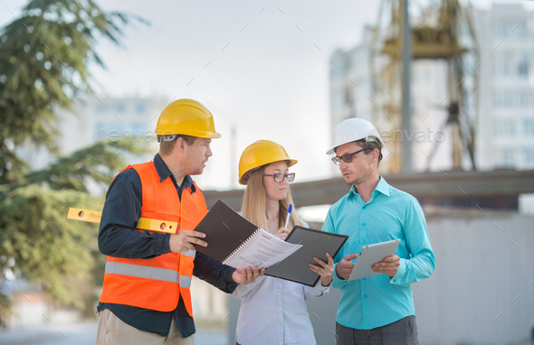 men and a woman in yellow and white helmets, blue shirts are standing at a construction site