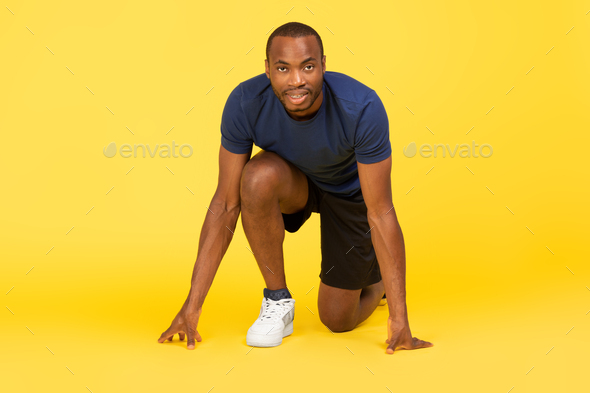 African Male Runner Standing In Crouch Start Position, Yellow Background
