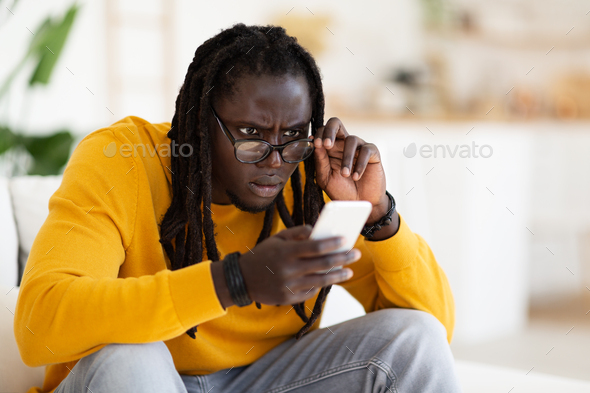 Bad Vision. Black Guy In Eyeglasses Looking At Smartphone Screen At Home