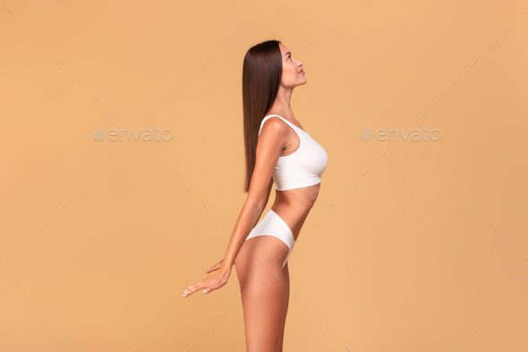 Profile side view shot of young fit lady with perfect ideal body shape  posing isolated on beige Stock Photo by Prostock-studio