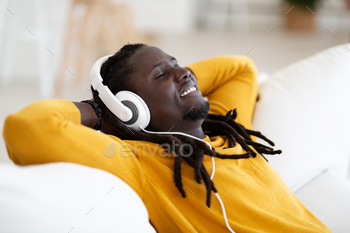 Relaxed Happy African American Guy In Headphones Listening Music At Home