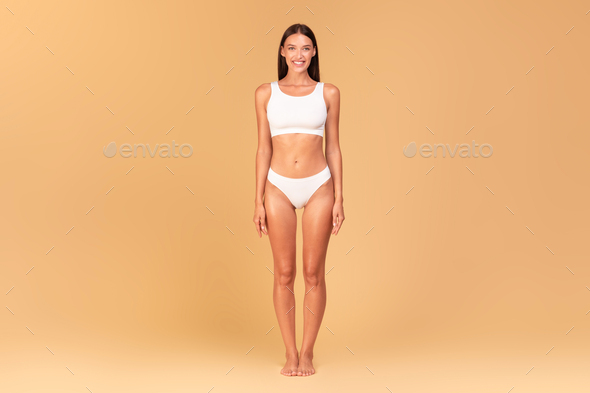 Full length frontal view of slim woman with perfect body shape and flat  tummy posing on beige studio Stock Photo by Prostock-studio