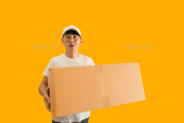 Young Asian delivery man wearing cap and white t-shirt holding parcel post box on yellow background