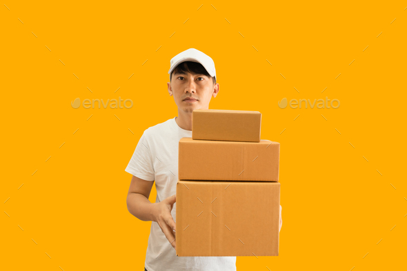 Young Asian delivery man wearing cap and white t-shirt holding parcel post box on yellow background