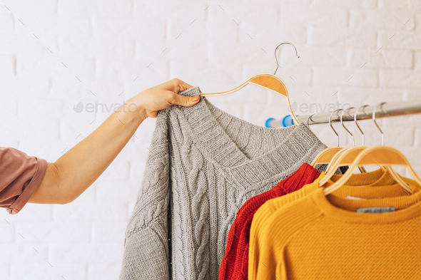 Woman's hand removes grey knitted jacket on wooden hanger from an iron rack rale