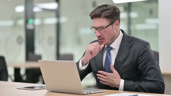 Sick Middle Aged Businessman with Laptop Coughing in Office alt