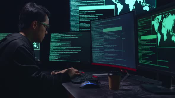 Asian Male Hacker Hacking With Multiple Computer Screens In Dark Room alt