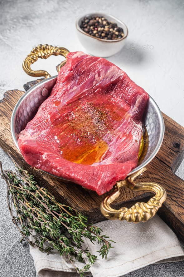 Flap or flank steak, raw beef meat in skillet with herbs and olive oil. White background. Top view