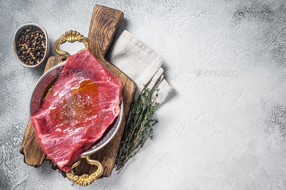 Flap or flank steak, raw beef meat in skillet with herbs and olive oil. White background