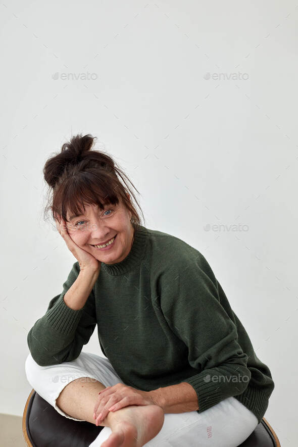 Cheerful elderly woman sitting on leather ottoman