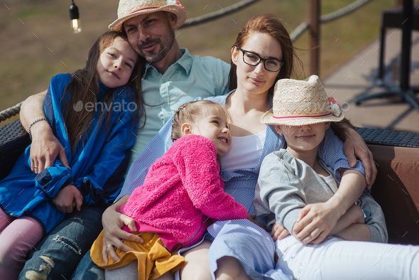 happy family with three daughters is enjoying a hot summer day sitting on terrace of a restaurant