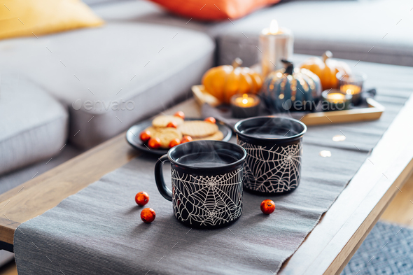 Cozy halloween plans at home. Hot tea drink in black mugs with spider net pattern, cookies