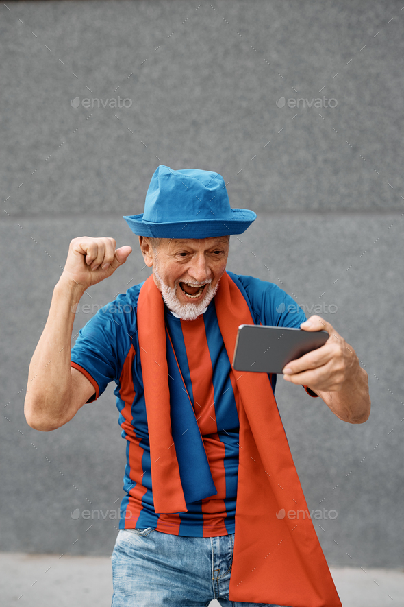 Cheerful senior soccer fan watching match over smart phone.