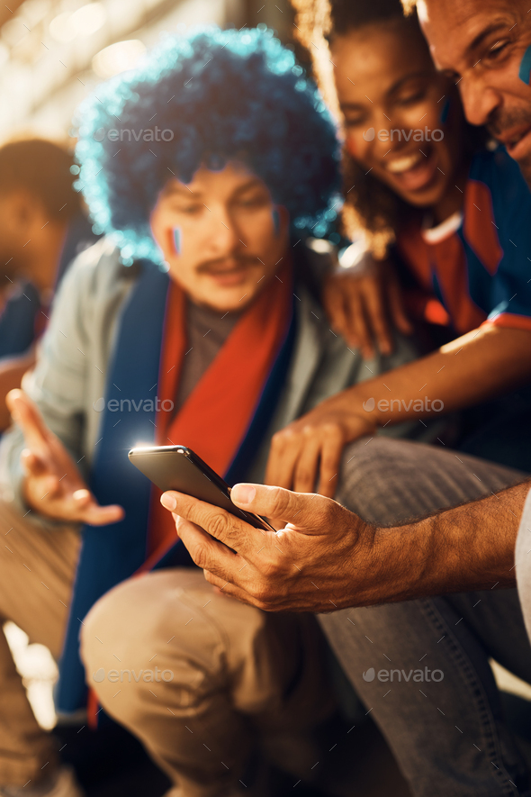 Close up of soccer fans watching live match broadcast on mobile phone.