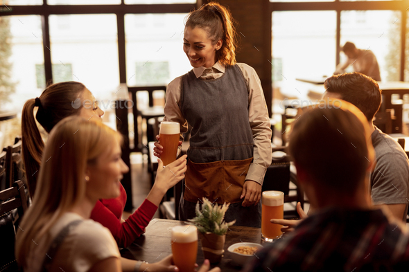 Happy waitress serving beer to group of friends in a bar.