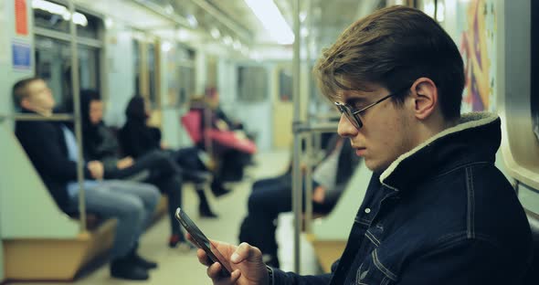 Fashionable Guy with Glasses is Riding in the Car and Looking at the Phone alt
