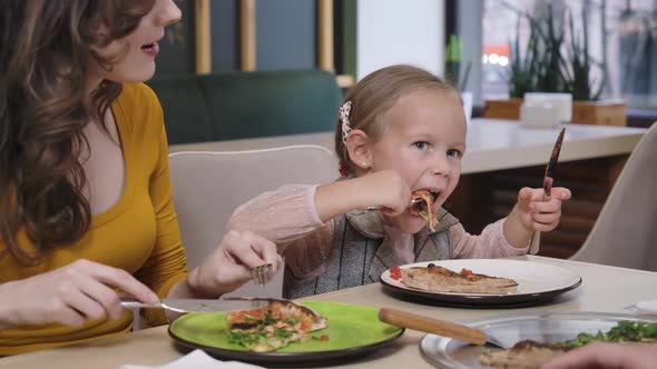 Portrait of Pretty Caucasian Daughter Eating Pizza in Restaurant Resting with Cheerful Mother alt