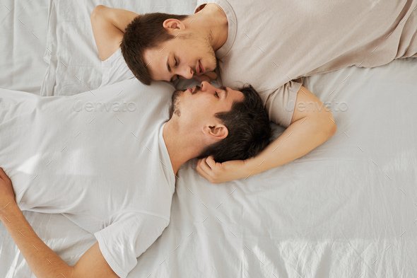 Young gay couple lying on bed head-to-toe, top view