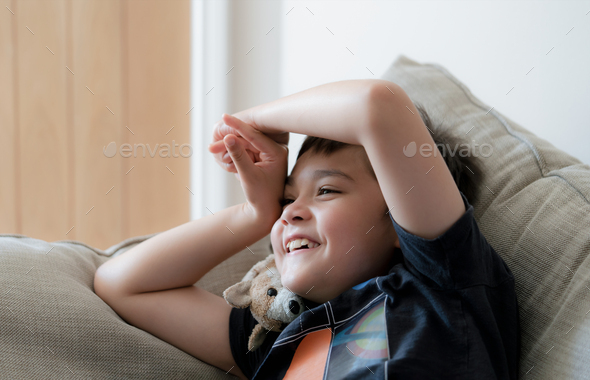 Portrait happy kid laughing, boy with big smile sitting on sofa having fun watching cartoon on TV