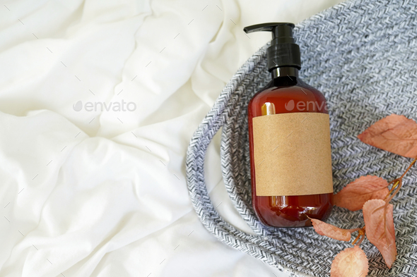 Brown pump cosmetic bottle with autumn leaves on white bed background. Cosmetic packaging mockup