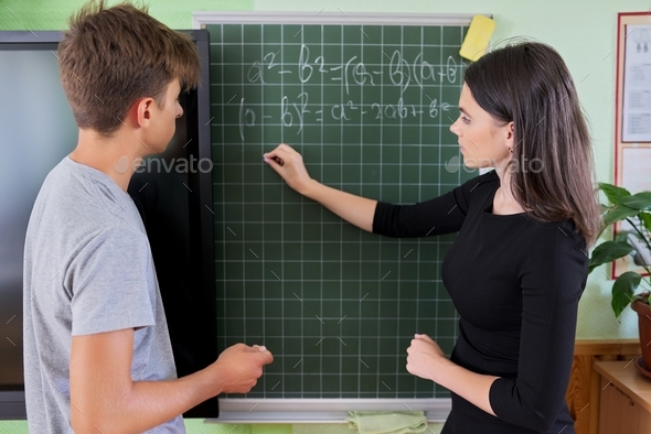 Male teenager student with teacher near school chalk board at math lesson