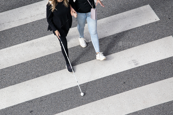 Scene of a Blind woman walking on zebra crossing helped by another person
